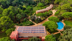 A large building with solar panels on the roof, surrounded by lush greenery and a swimming pool. - Albamar Apartaments (Lloret de Mar)