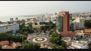 Un paisaje urbano con una combinación de edificios residenciales y comerciales, una glorieta central y una masa de agua al fondo.