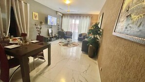 Un salón amplio con comedor, un televisor de pantalla plana montado en la pared, un ventilador de techo y un cuadro grande en la pared.