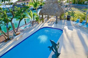 A swimming pool with a dolphin statue, surrounded by lounge chairs and a thatched umbrella.