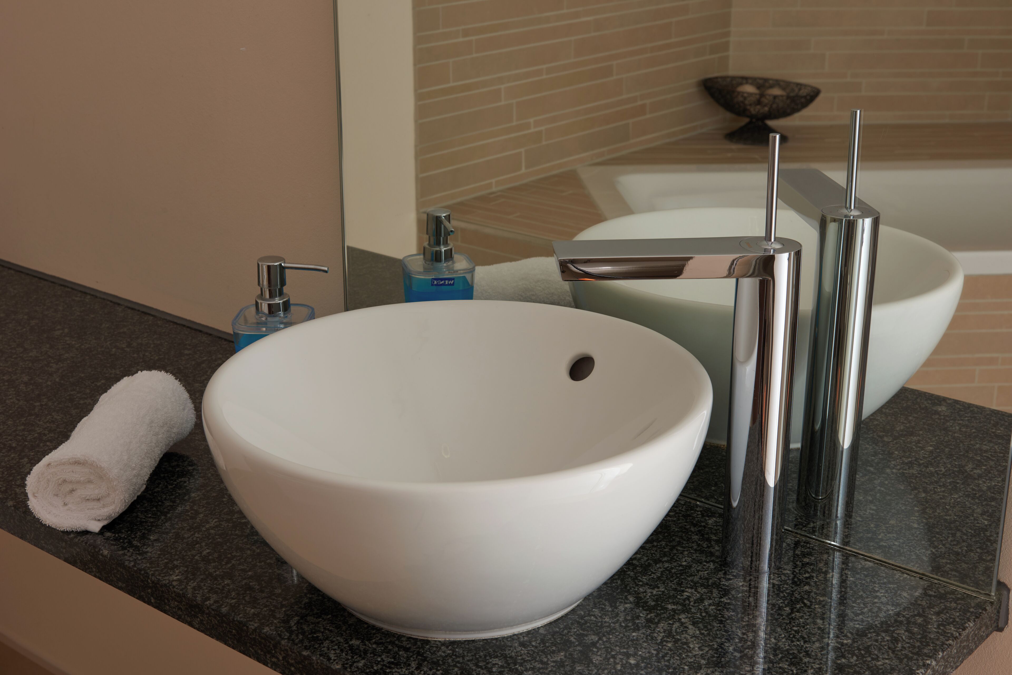 A modern bathroom with a white sink, chrome faucet, and a towel on the counter.