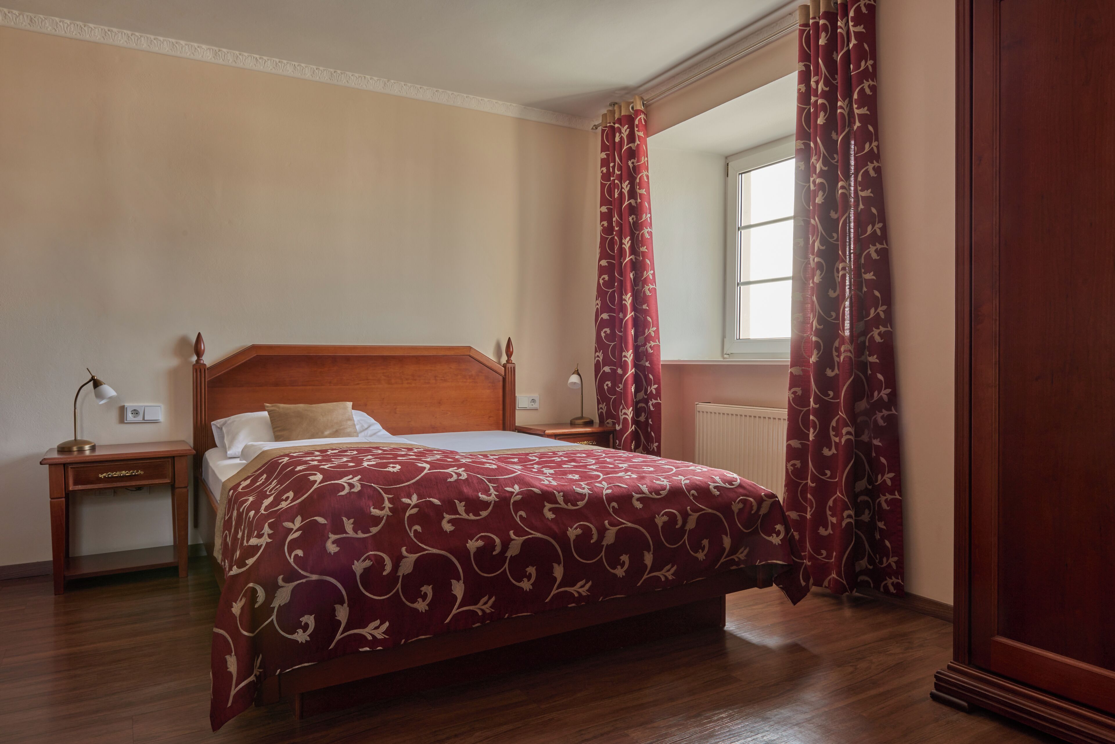 A bedroom with a wooden bed, a nightstand, a lamp, and a window with curtains.