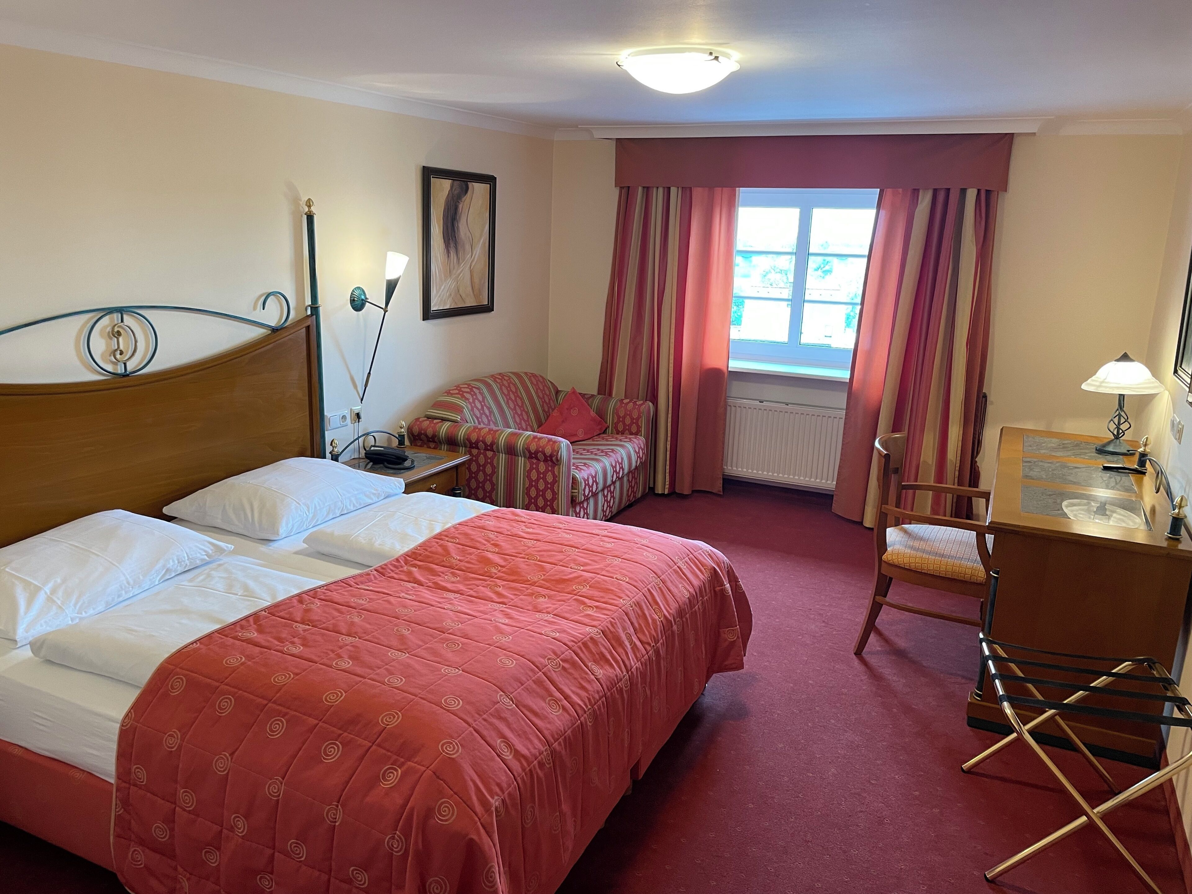 Une chambre d’hôtel avec deux lits, un bureau, une chaise, un radiateur et une fenêtre avec des rideaux.