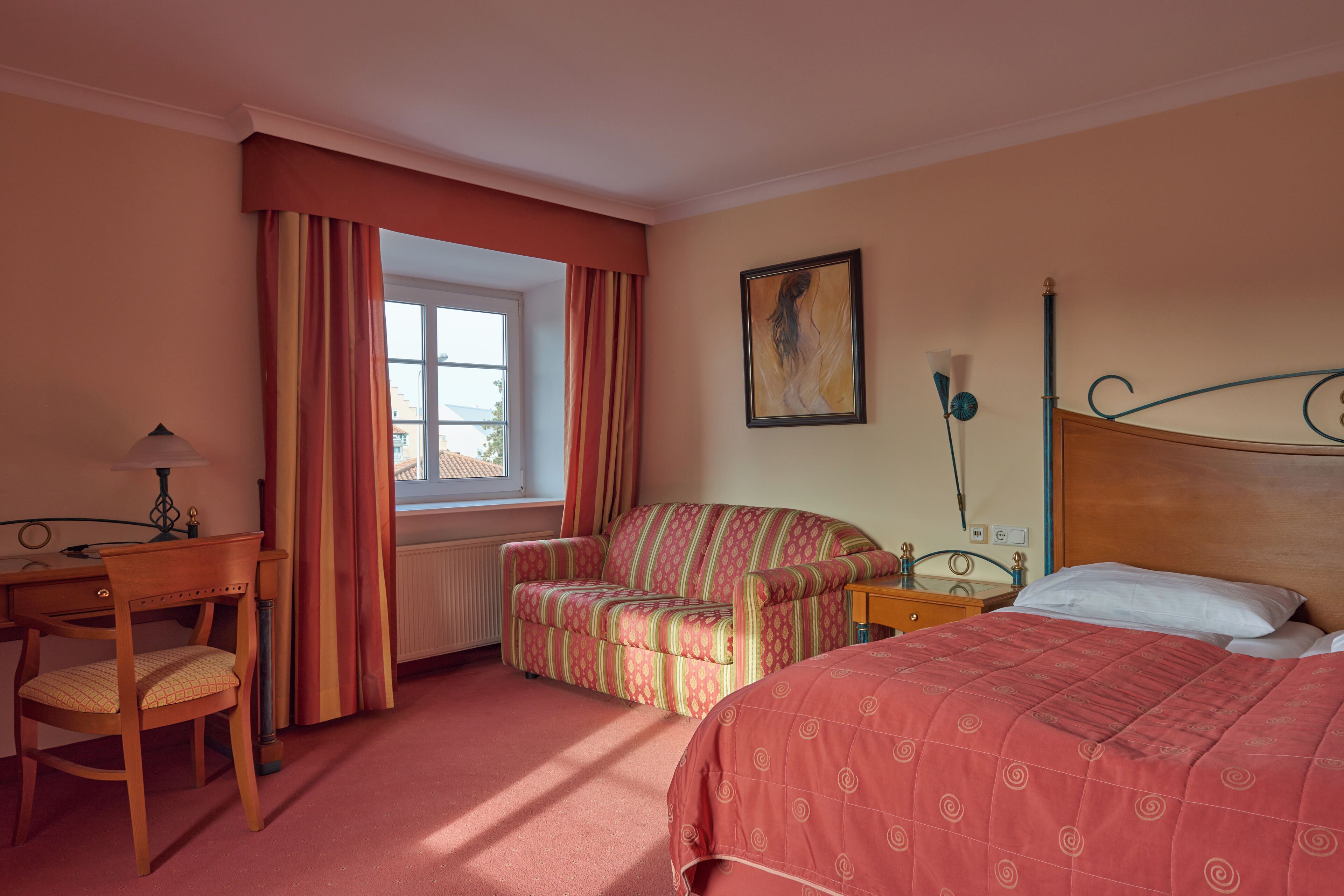 Une chambre d’hôtel avec un lit, une chaise, un canapé, un bureau et une fenêtre avec des rideaux.