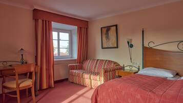 Une chambre d’hôtel avec un lit, une chaise, un canapé, un bureau et une fenêtre avec des rideaux.