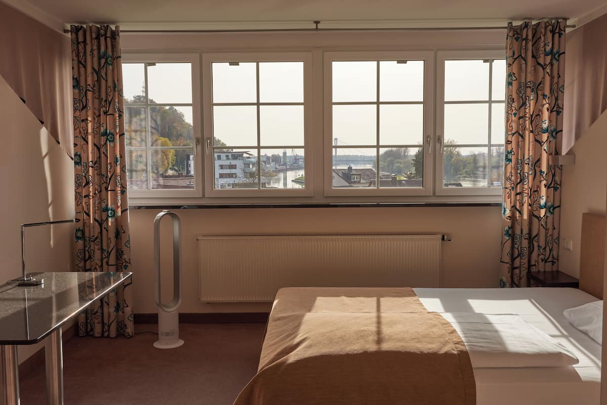 Una habitación de hotel con cama, escritorio, radiador y ventana con cortinas.