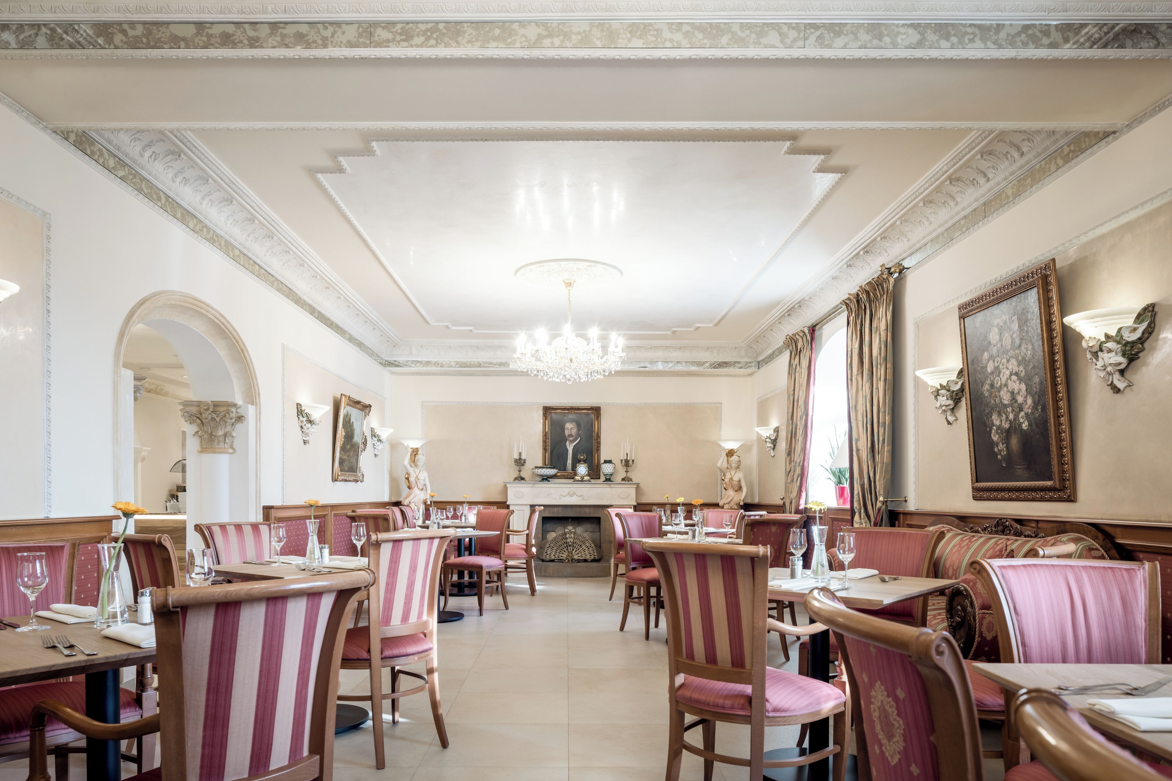Une salle à manger élégante, avec des chaises à motifs rayés, un lustre et des œuvres d’art encadrées accrochées aux murs.