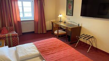 Una habitación de hotel con cama, escritorio, silla, televisor y radiador.