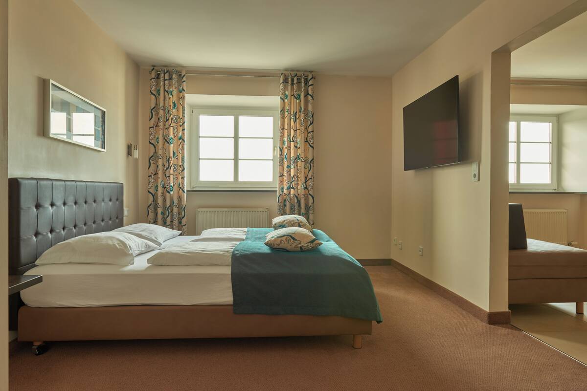 Habitación de hotel con una cama grande, televisor de pantalla plana, ventana con cortinas y un espejo.