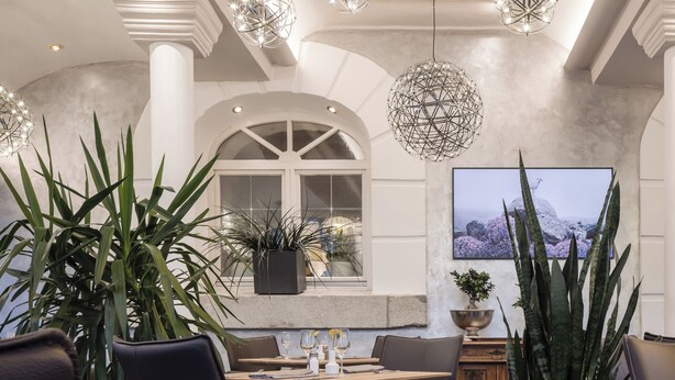 Un espace repas moderne agrémenté de luminaires suspendus aux formes géométriques, d’un grand téléviseur à écran plat et de plantes en pot.