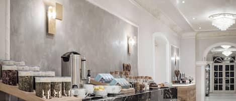 Un moderno vestíbulo de hotel con un mostrador de recepción de mármol, una estación de café y una araña.