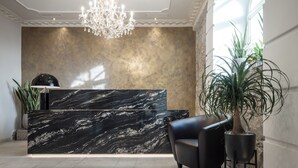 Un espace d’accueil doté d’un comptoir de réception en marbre, d’un lustre, d’une plante en pot et d’un fauteuil moderne.