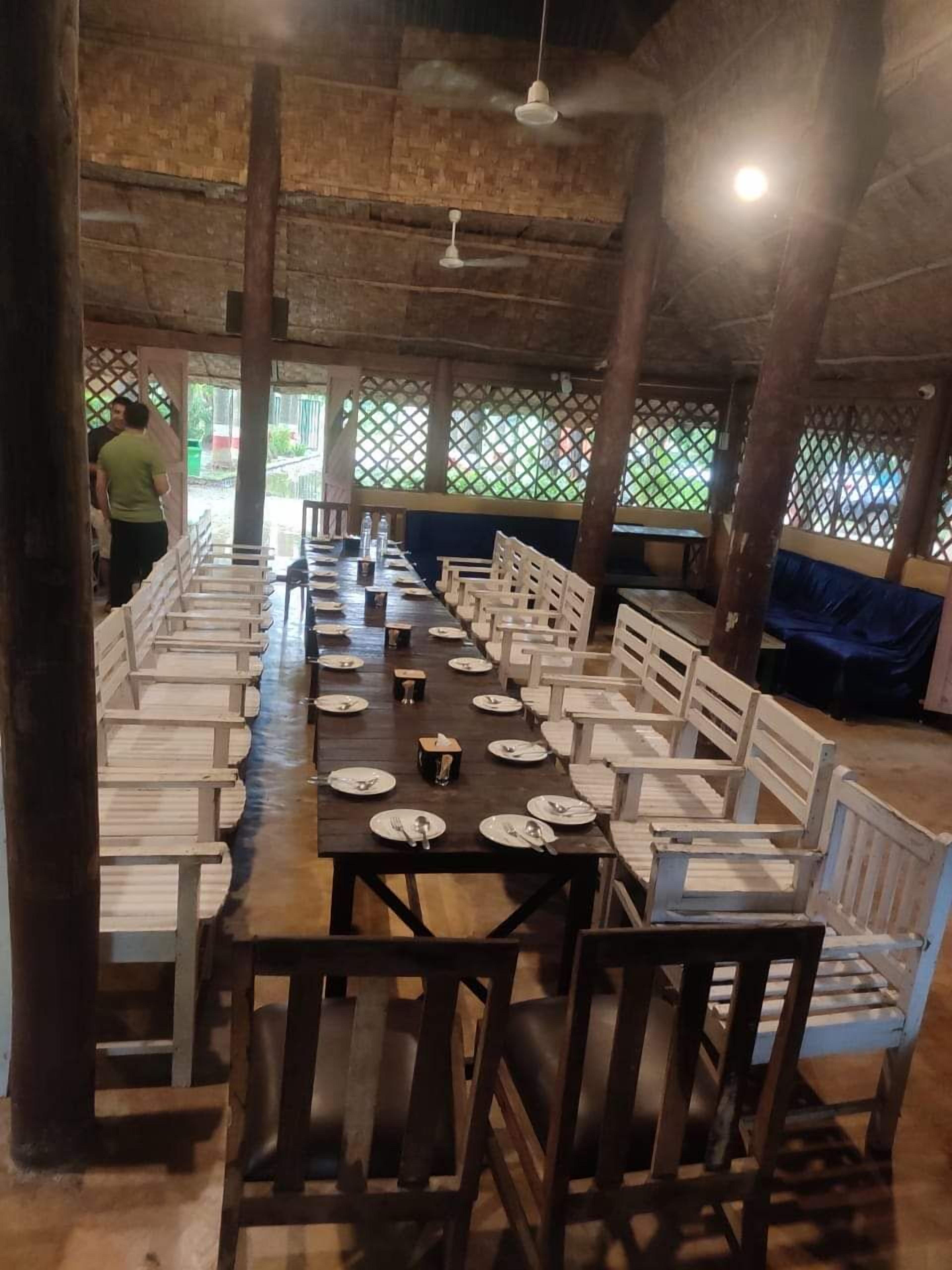 Een lange eettafel met stoelen, een plafondventilator en uitzicht door een traliewerkraam.