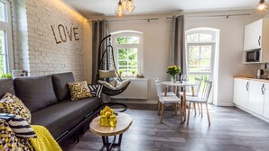 A modern living room with a sofa, a hanging chair, a dining table with chairs, and a kitchen area with a microwave.