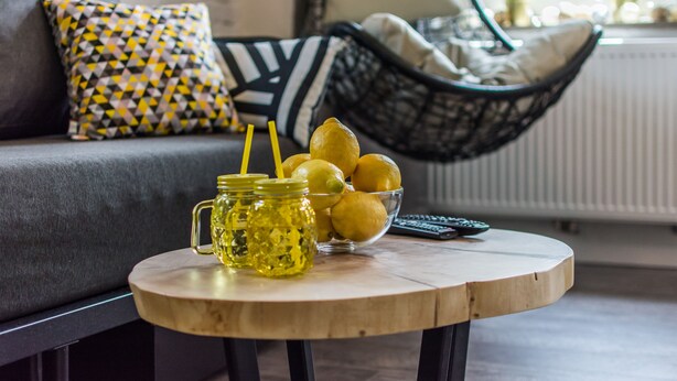 A round wooden table with a glass jar, lemons, and a remote control.