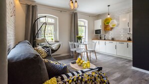 A modern living room with a sofa, a hanging chair, a dining table with chairs, and a kitchen area with cabinets and appliances.