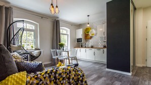 A modern living room with a hanging chair, a dining area with a table and chairs, and a kitchen with white cabinets and a black accent wall.