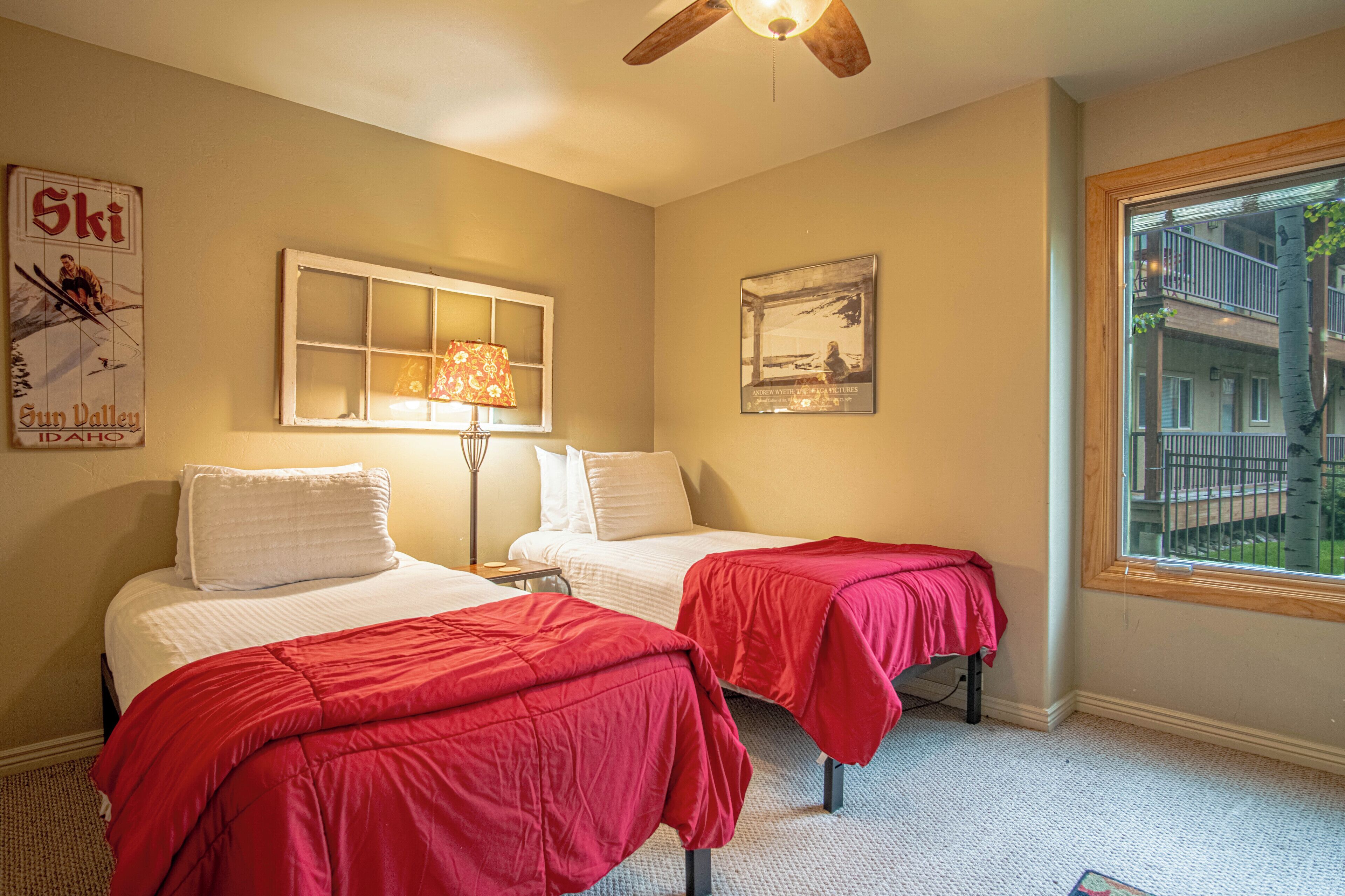 A hotel room with two beds, a window with a view, a ceiling fan, and a lamp.