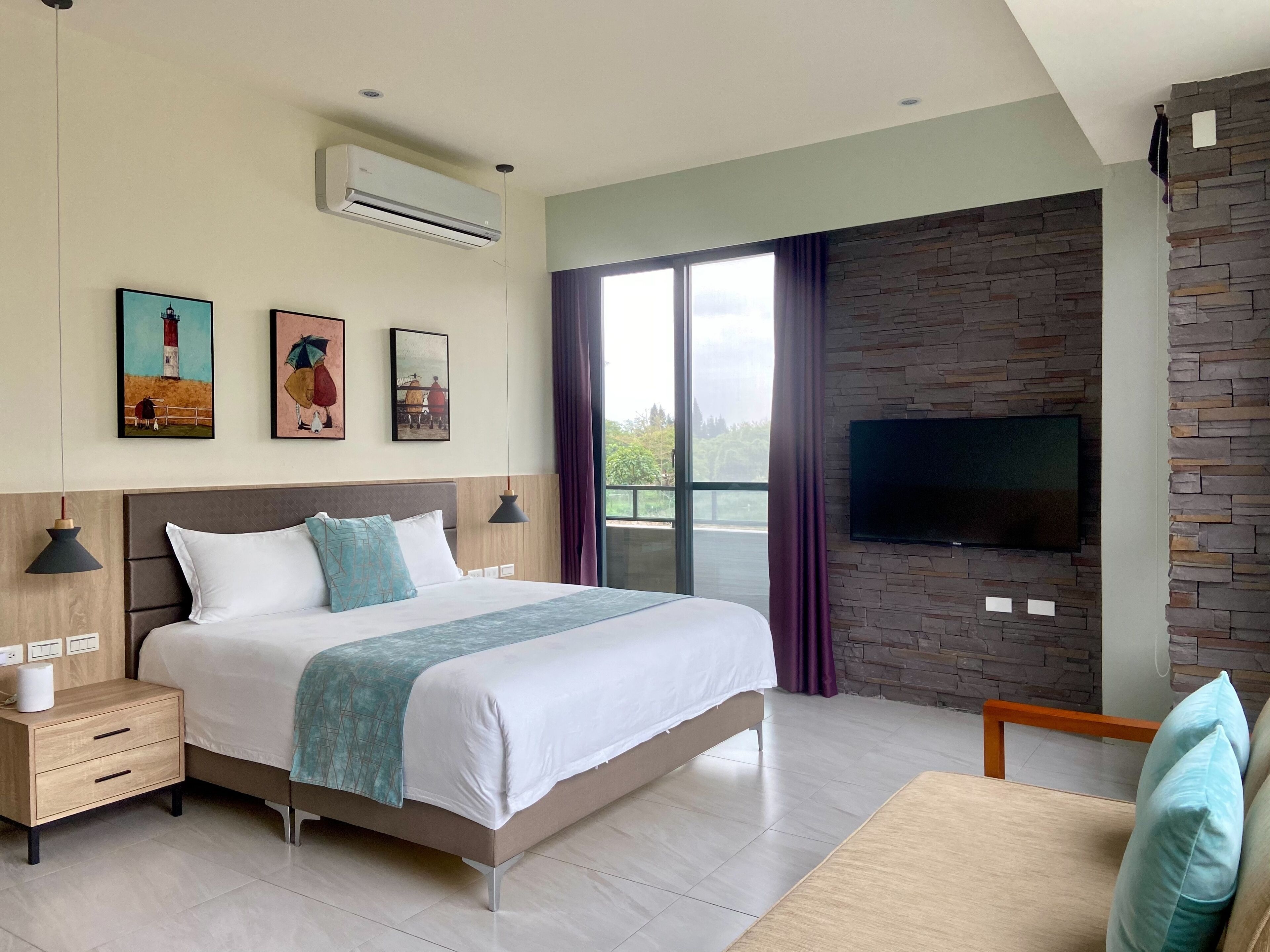 Ein modernes Hotelzimmer mit einem großen Bett, einem an einer Steinwand montierten Fernseher und Kunstwerken an der Wand.