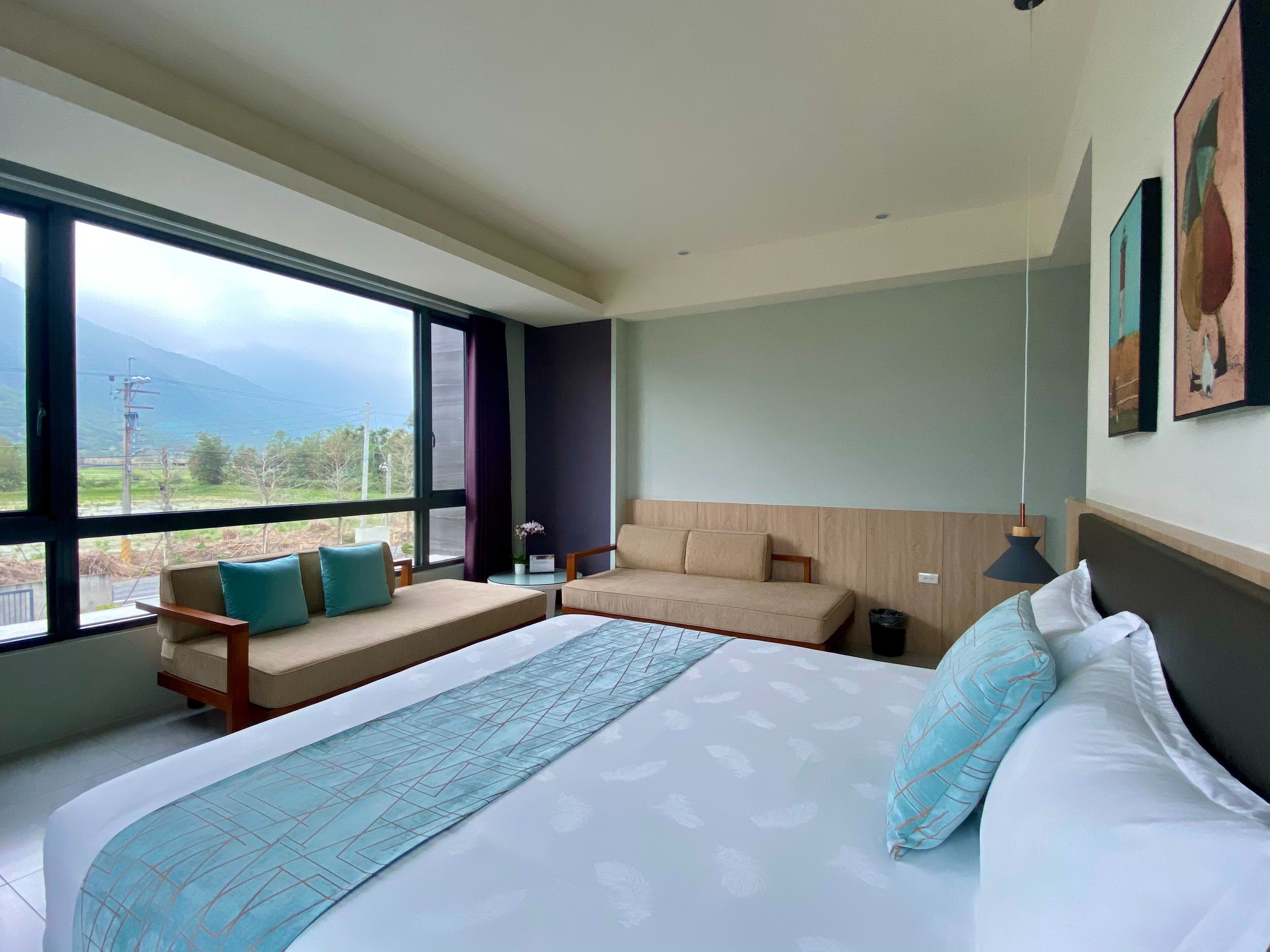 A modern hotel room with a large bed, a sofa, a small table, and a view of the outdoors.