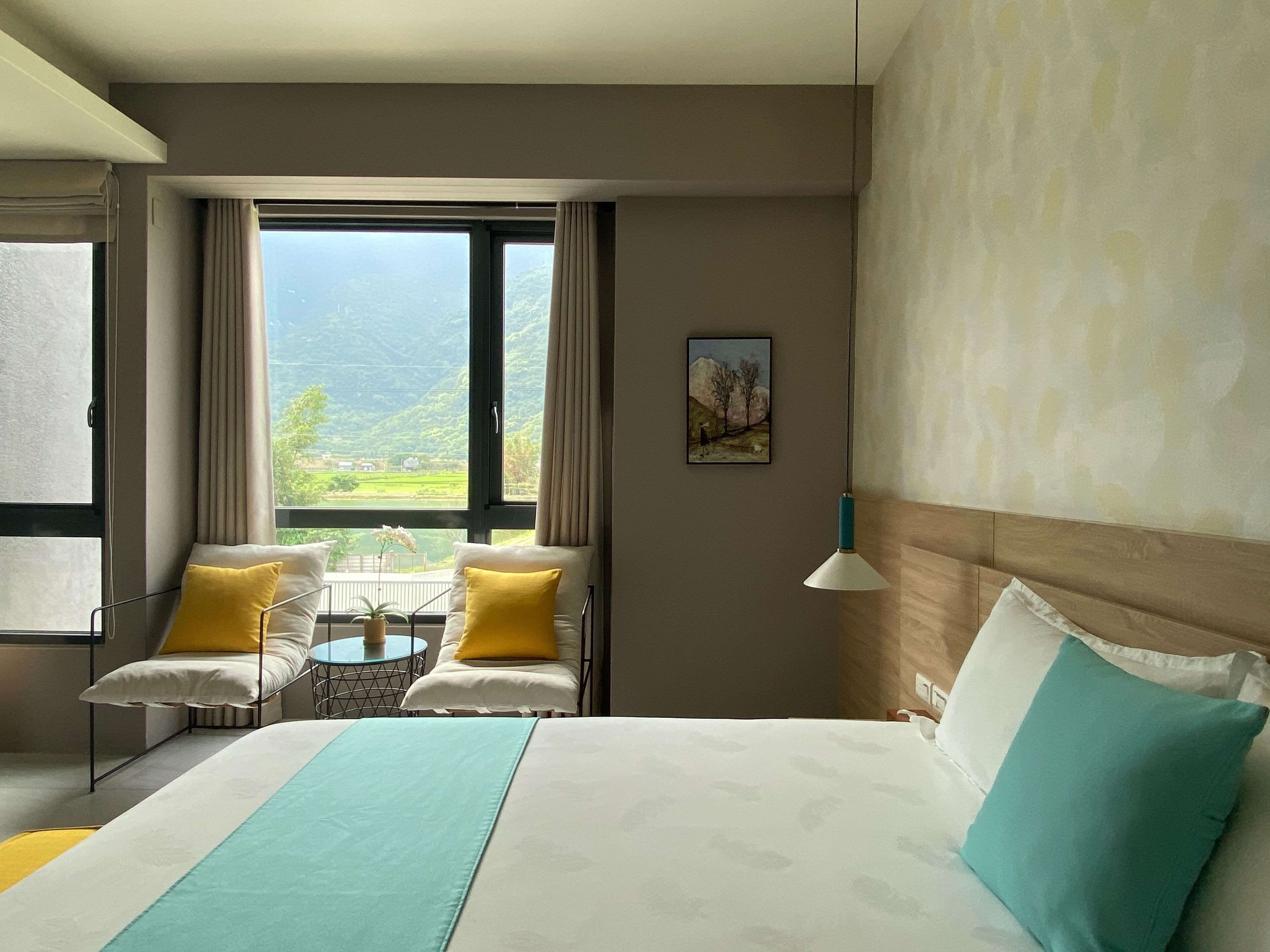 A hotel room with a bed, a small table, two chairs, and a view of a mountainous landscape.