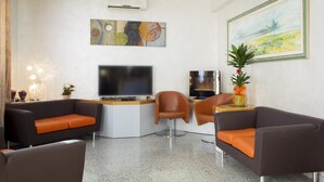 A modern living room with a flat-screen TV, two sofas with orange cushions, a coffee table, and a painting on the wall. - Hotel San Marco (Rionero in Vulture)