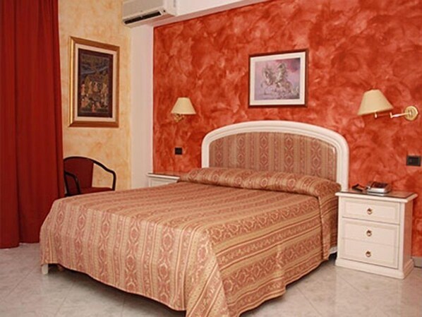 A bedroom with a patterned bedspread, a white headboard, two bedside tables with lamps, and a red curtain.
