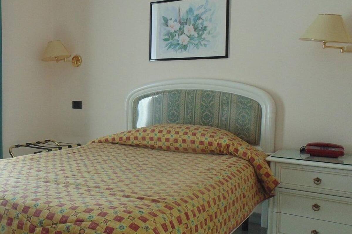 A bedroom with a bed, a bedside table, a lamp, and a framed picture on the wall.