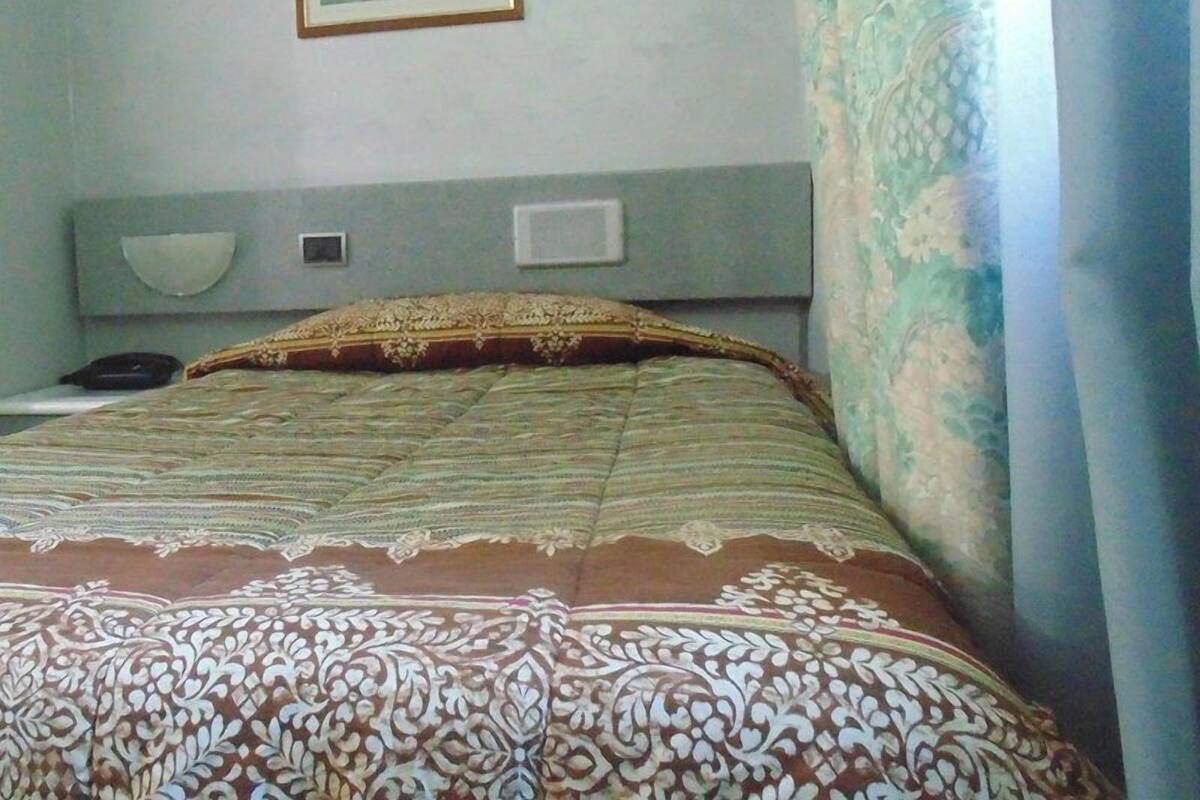 A hotel room with a bed, a bedside table, a lamp, and a painting on the wall.
