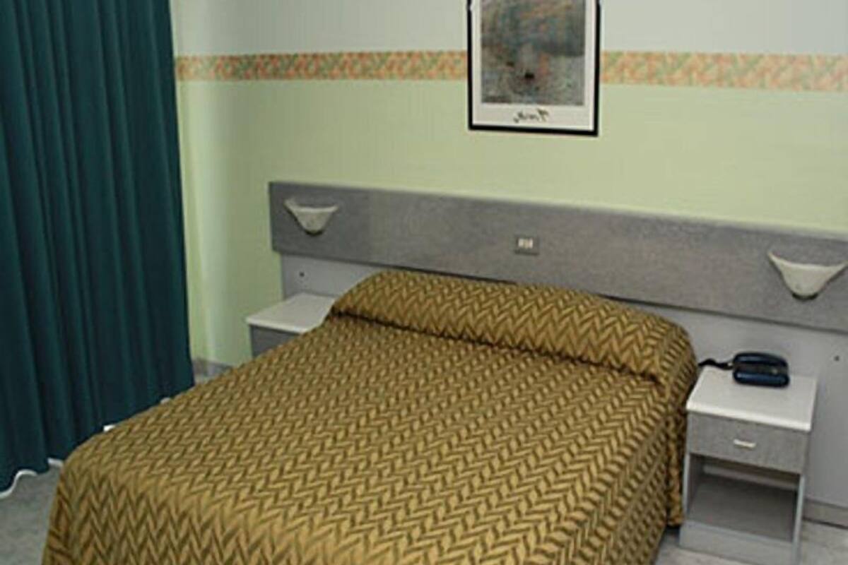 A hotel room with a bed, a nightstand, a bedside table, a lamp, and a framed picture on the wall.