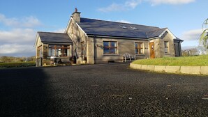 A stone house with a sloped roof, a chimney, and a flag. - Carnately Lodge Ballycastle (Ballycastle)