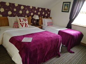 A hotel room with two beds, each with white bedding and a purple throw blanket. There are decorative pillows with the word "LOVE" on one bed. A lamp and a framed picture are on the nightstand. - Carnately Lodge Ballycastle (Ballycastle)