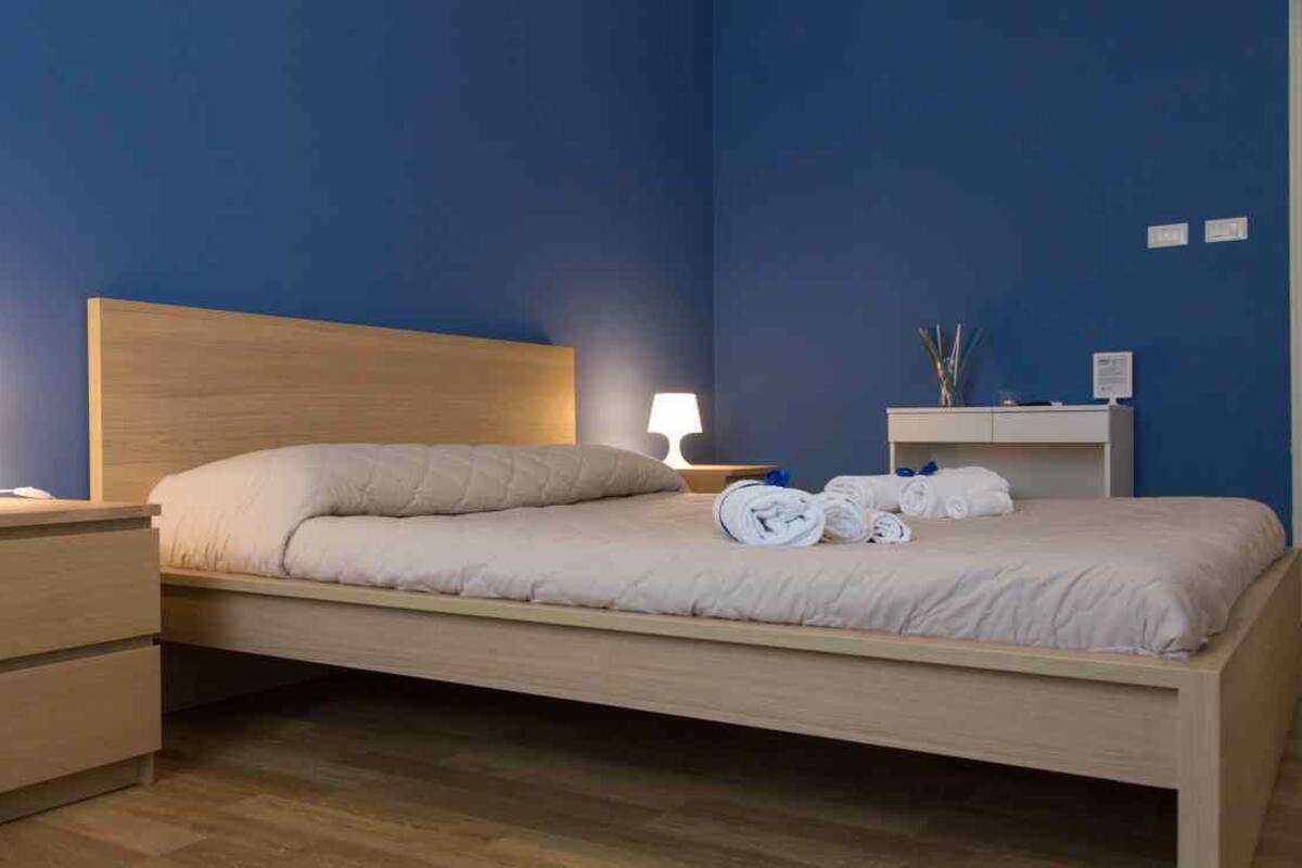 A neatly made bed with a wooden headboard, two bedside tables with lamps, and a small bedside table with a vase and a clock.