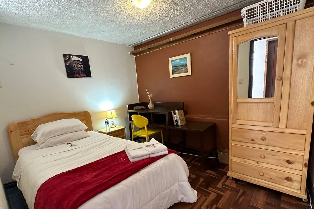 Un dormitorio con cama de madera, un escritorio con silla, un armario y un espejo.