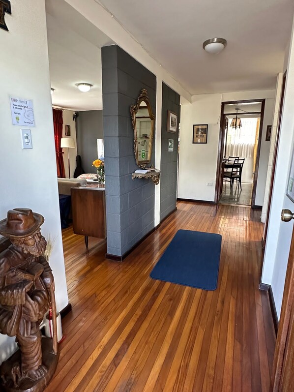 A hallway with wooden flooring, a blue mat, a mirror on a wall, and a statue. - St. Gallen Haus (Quito)