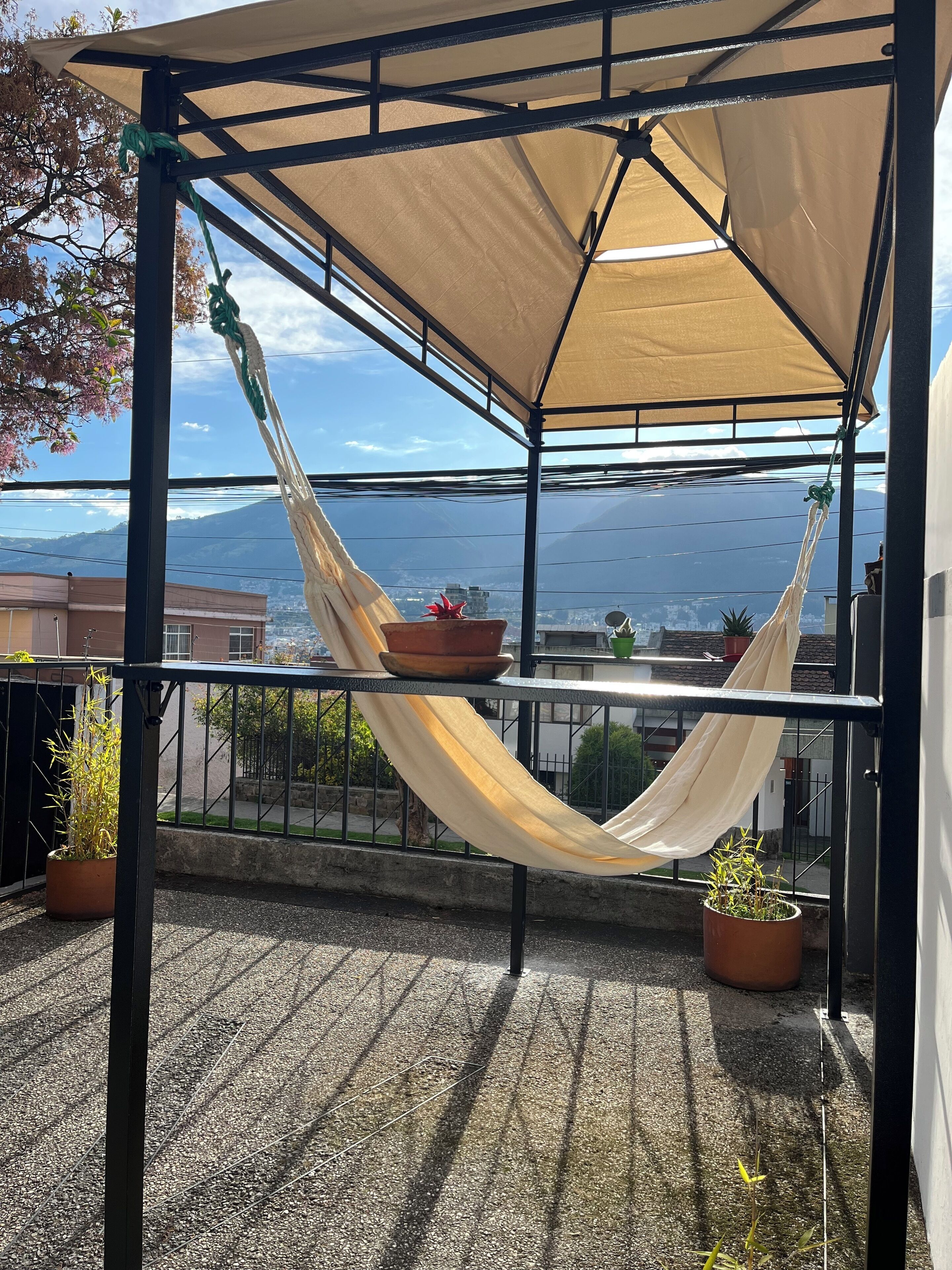 A balcony with a hammock, potted plants, and a view of a cityscape and mountains.