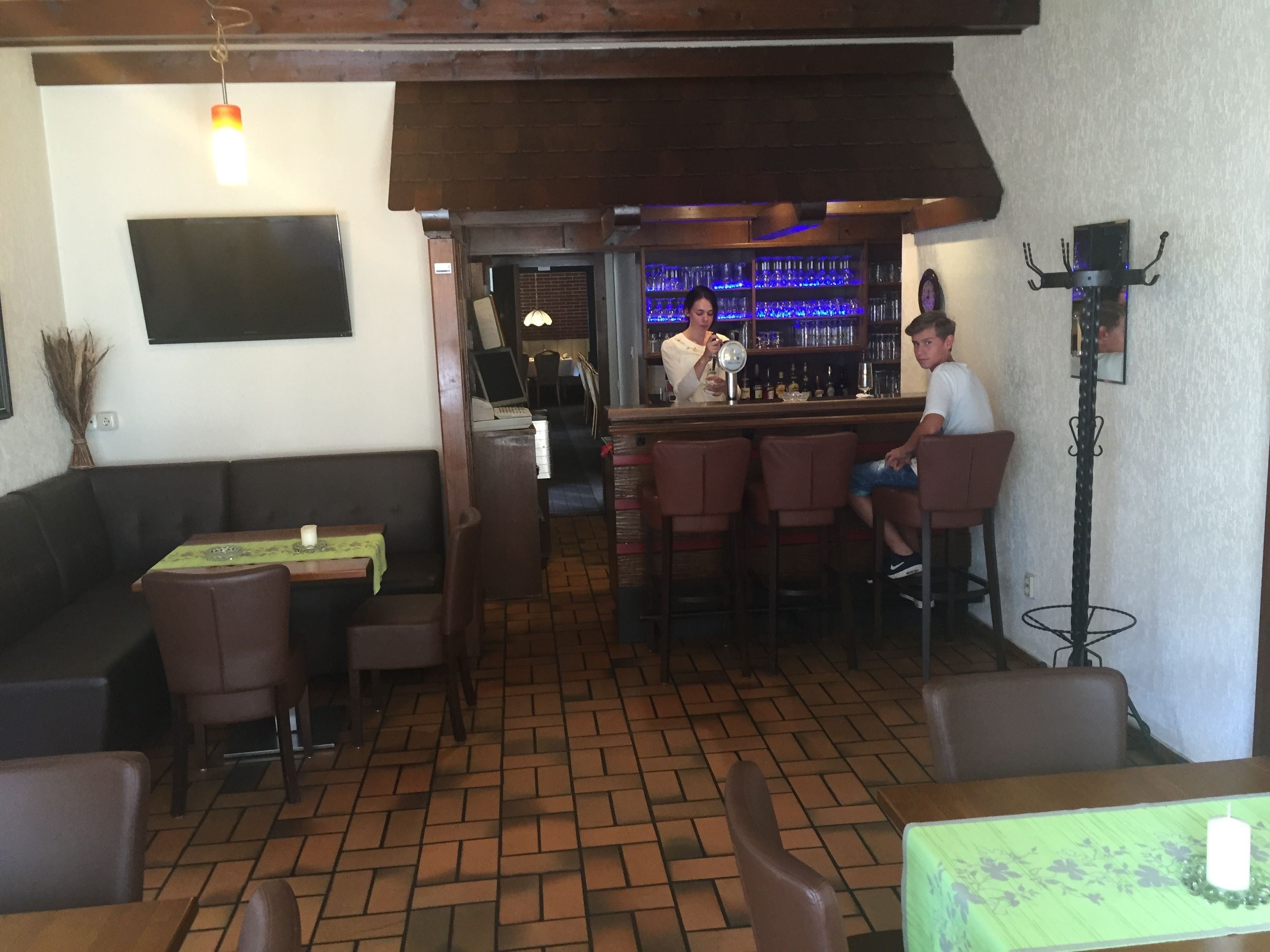 A restaurant with a bar area, wooden furniture, and tiled flooring.