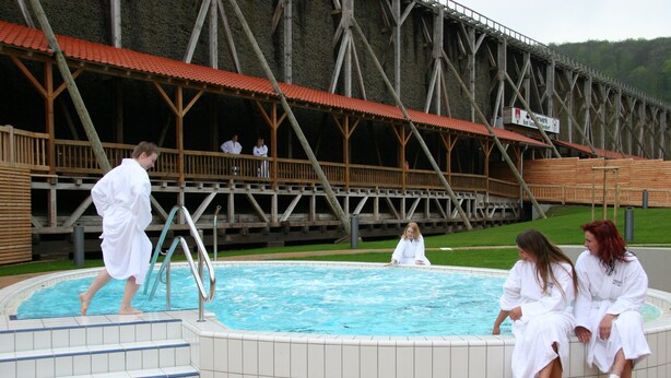 Ein Schwimmbeckenbereich mit einer Holzterrasse und einer großen Holzkonstruktion im Hintergrund.