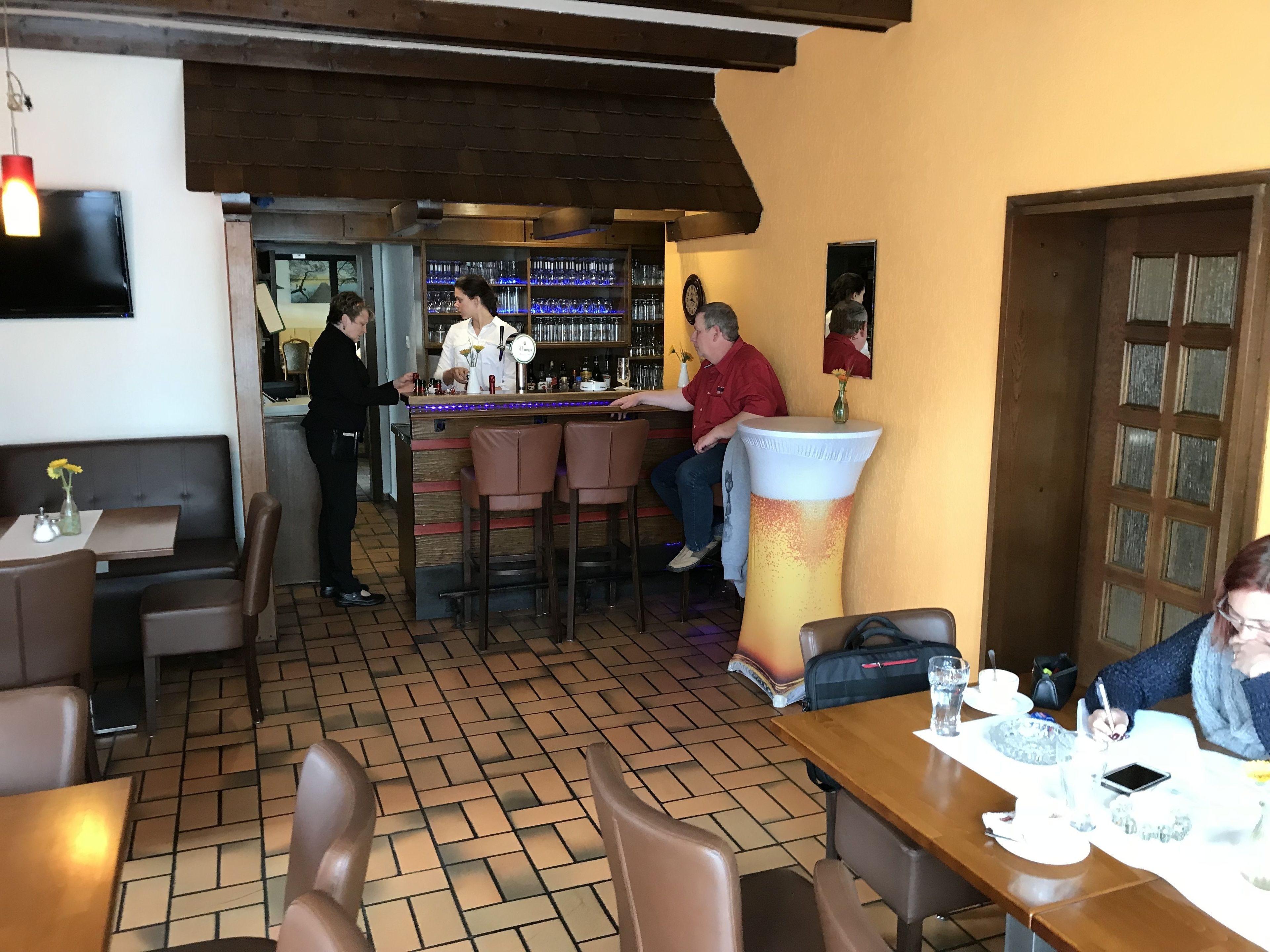 A restaurant interior with brick flooring, wooden bar counter, and bar stools.