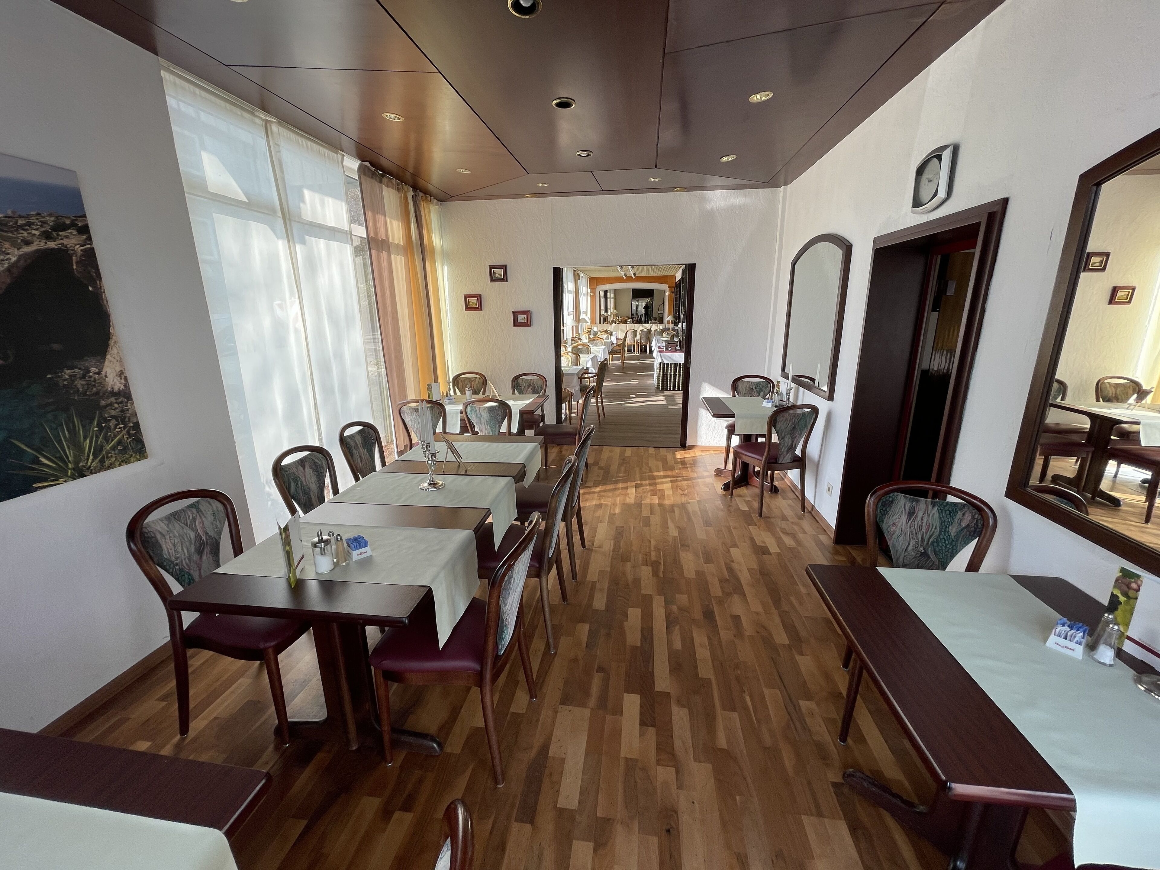 Un restaurante con piso de madera, manteles blancos y sillas de madera oscura.