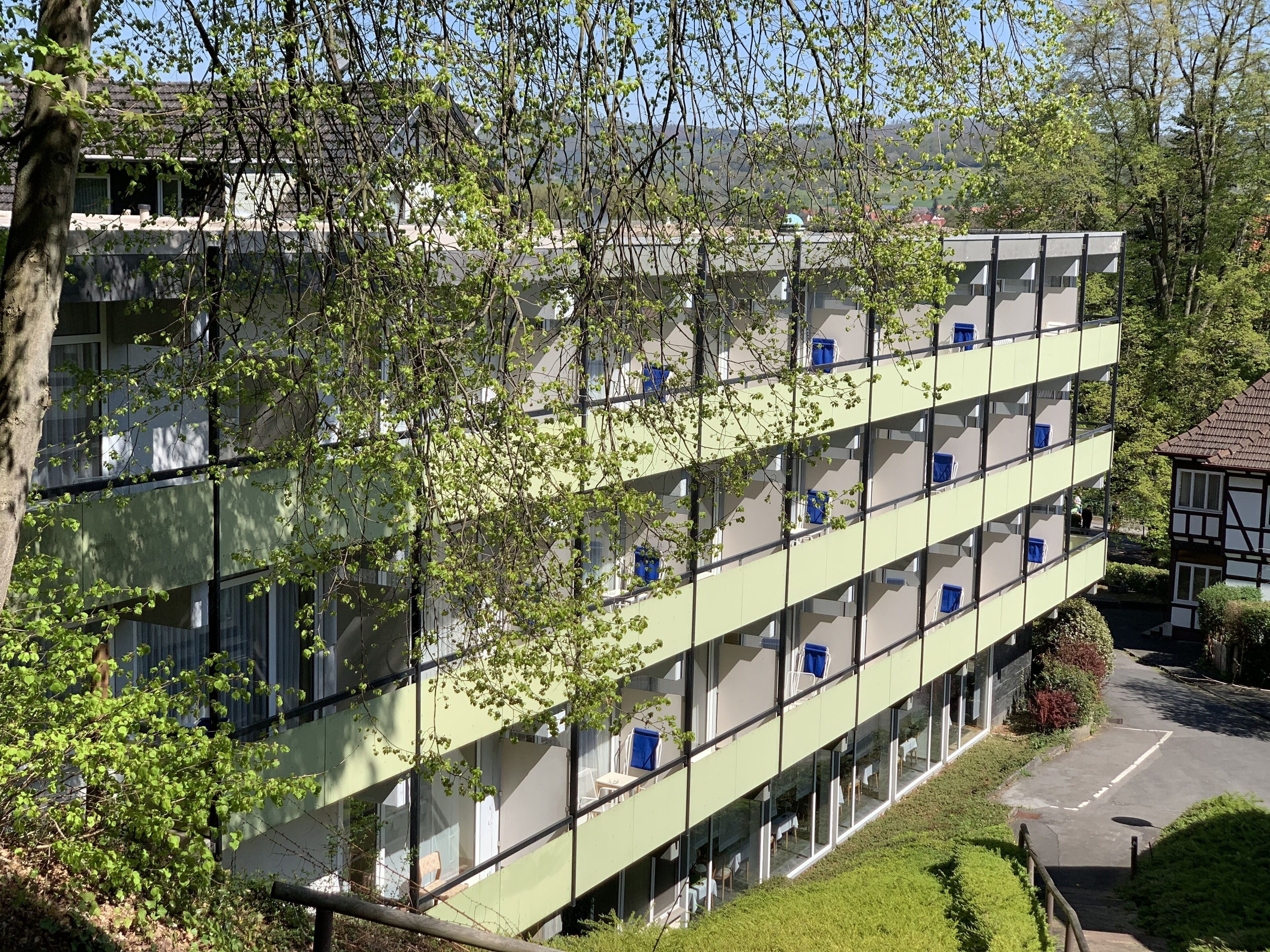 A multi-story building with balconies, surrounded by greenery.