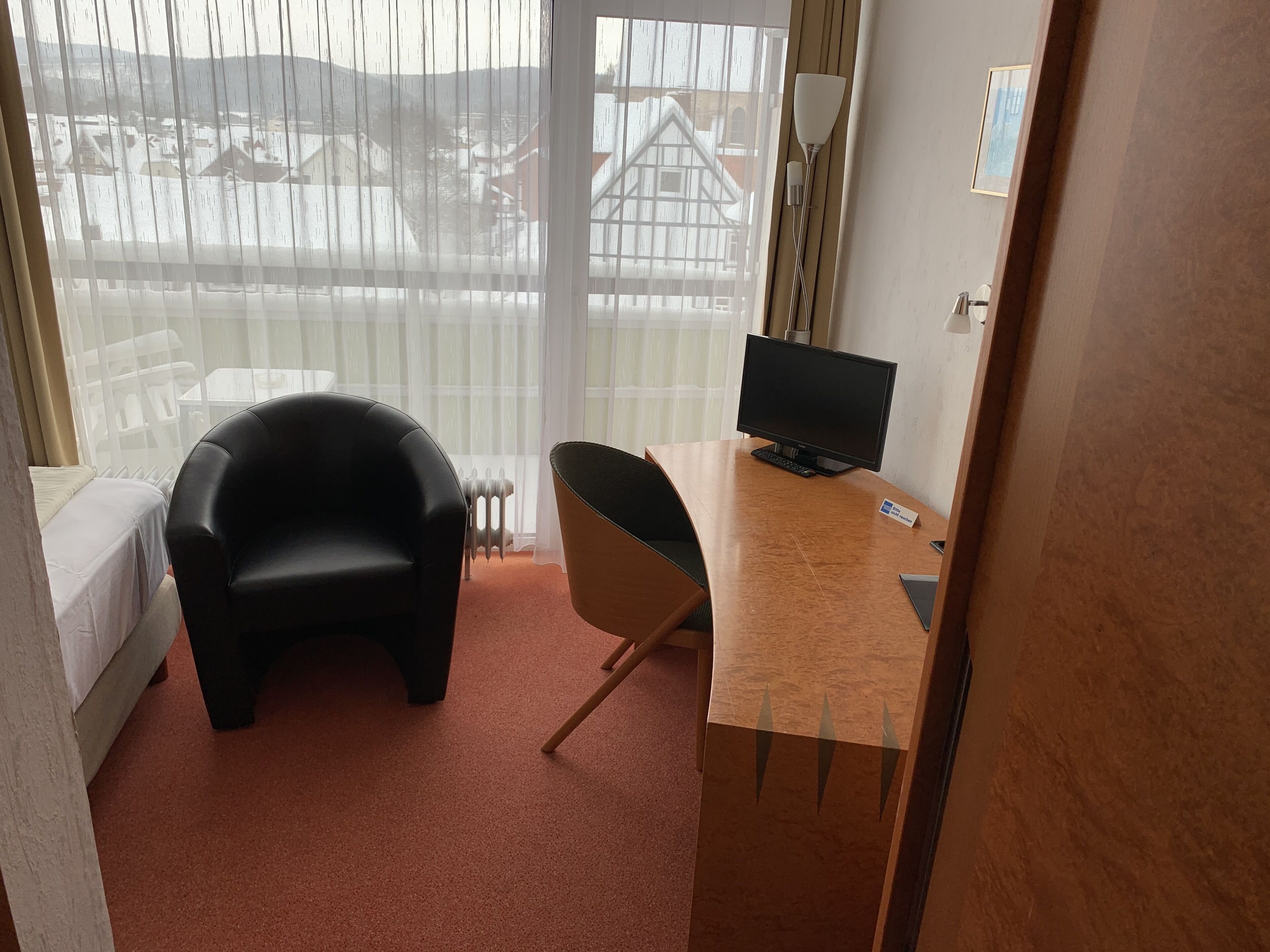 A hotel room with a bed, a desk with a computer, a chair, and a radiator.