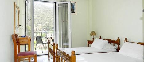 Une chambre avec un lit en bois, un bureau avec une chaise, une télévision et un balcon donnant sur la campagne.
