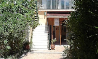 Entrada de hotel com uma escadaria que leva à porta, rodeada por vegetação.