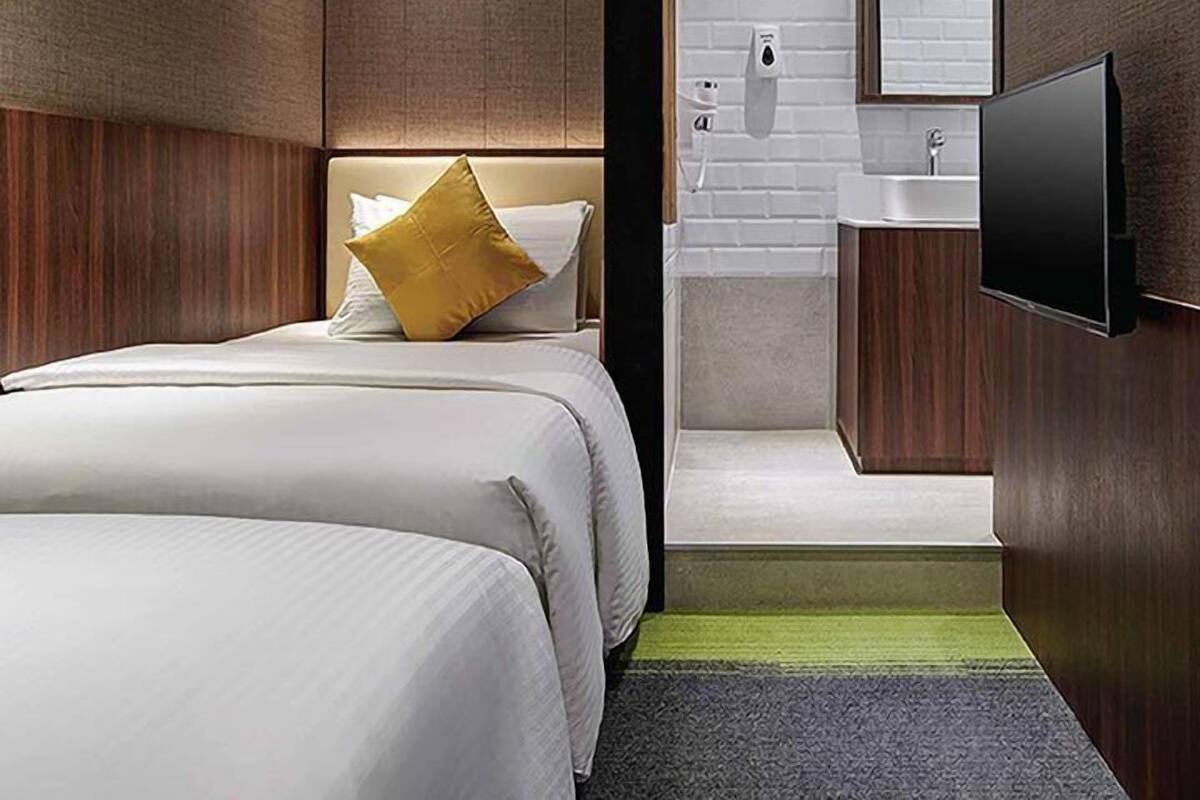 Una habitación de hotel moderna con cama, televisor, baño con lavamanos y espejo.