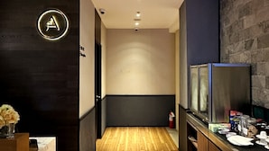 A hallway with a wooden floor, a reception desk with a logo, a stone wall, and a counter with various items. - Aerotel Cebu (Lapu-Lapu)