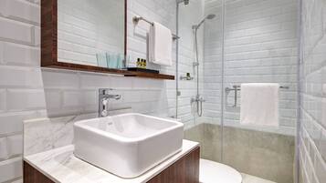 A modern bathroom with a white sink, mirror, and glass shower enclosure.