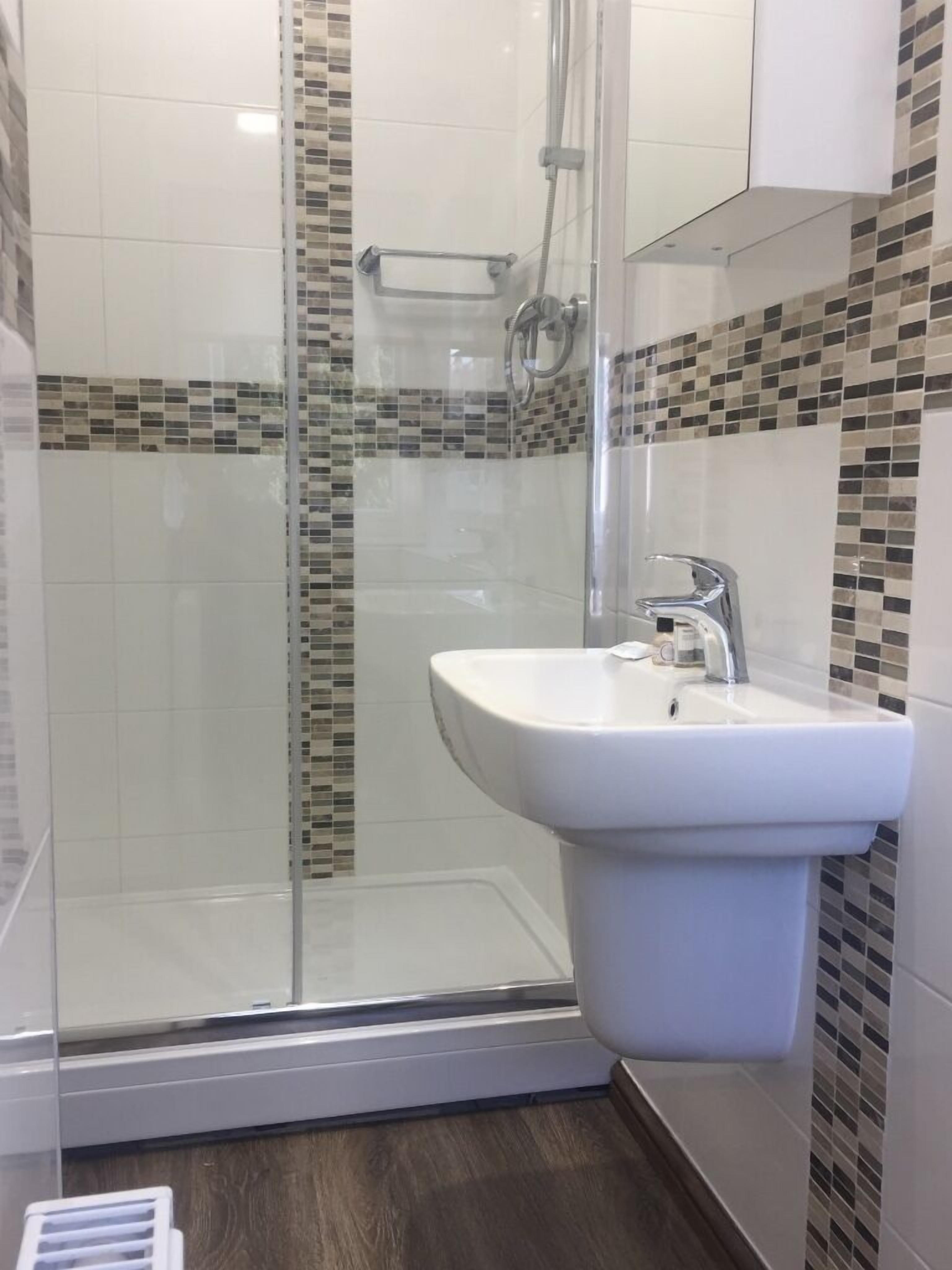 Une salle de bain moderne avec une douche à parois de verre, un lavabo blanc et des murs recouverts de mosaïques.