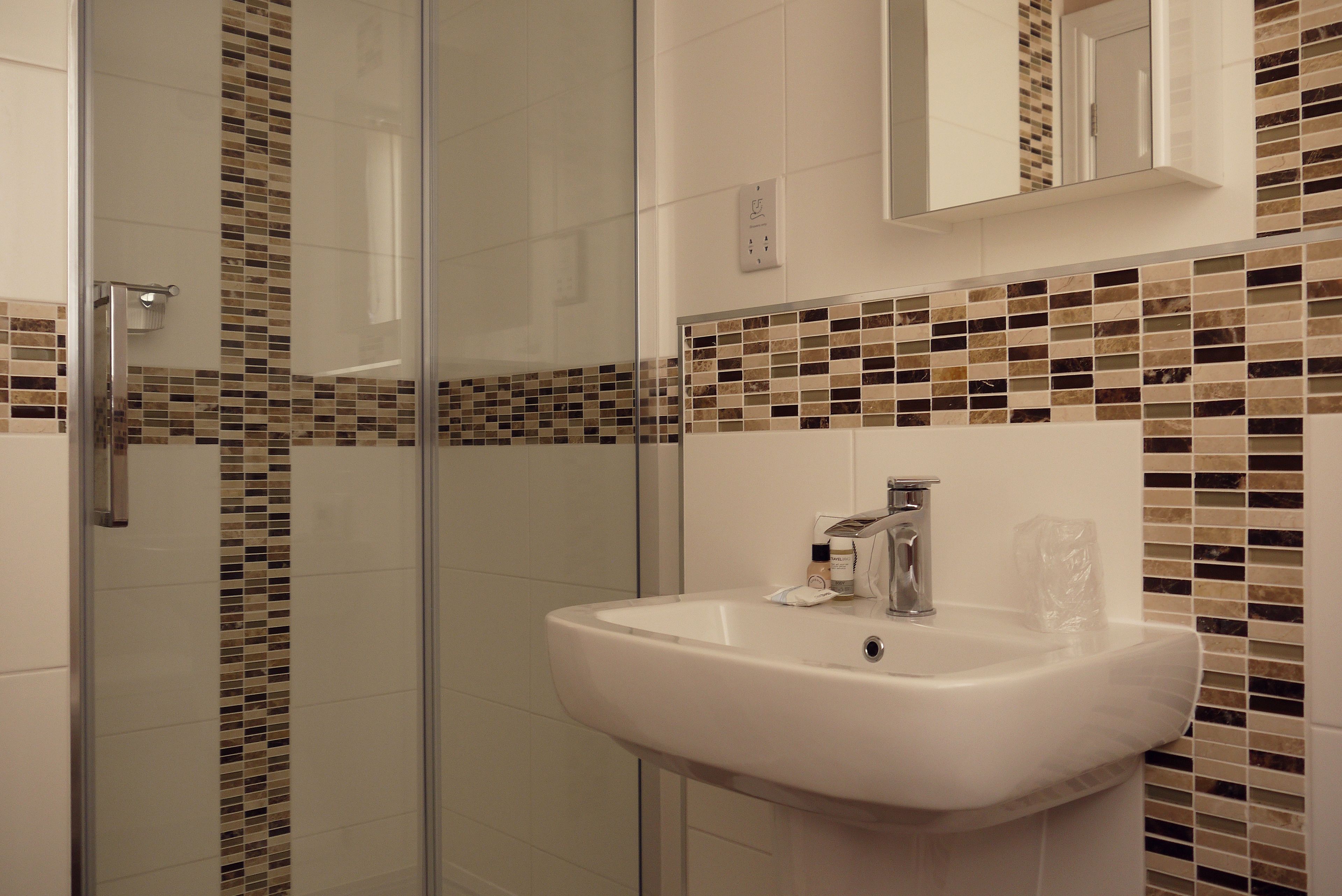 A bathroom with a glass shower enclosure, a white sink, and mosaic tile backsplash.