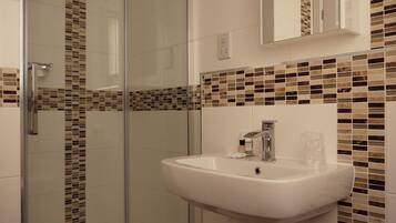 A bathroom with a glass shower enclosure, a white sink, and mosaic tile backsplash.